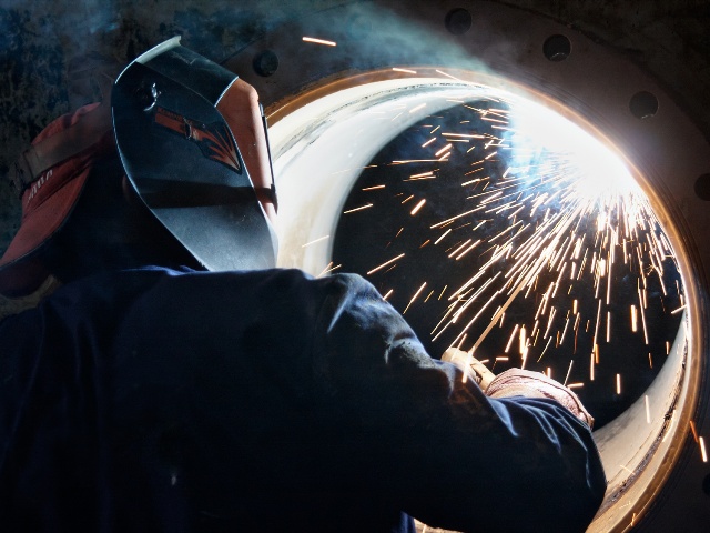 A metalworker welding a metal barrel